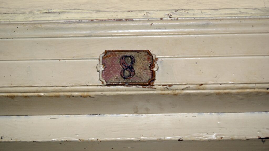 Tabliczka z numerem mieszkania, drzwi na klatce schodowej skrzydła od strony ulicy Wilczej. Fot. Monika Wesołowska, 2020, źródło: lapidarium detalu.