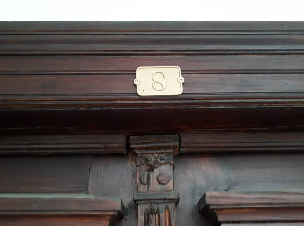 Numer na drzwiach do mieszkania na klatce schodowej od strony ulicy Mokotowskiej. Fot. Robert Marcinkowski, 2020, źródło: lapidarium detalu.