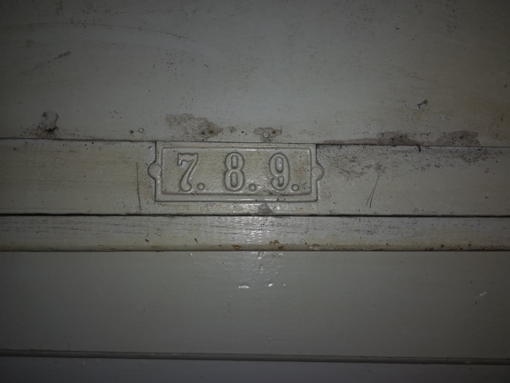 Tabliczka z numerami na drzwiach, klatka schodowa. Fot. Anna Laskowska, 2019, źródło: lapidarium detalu.