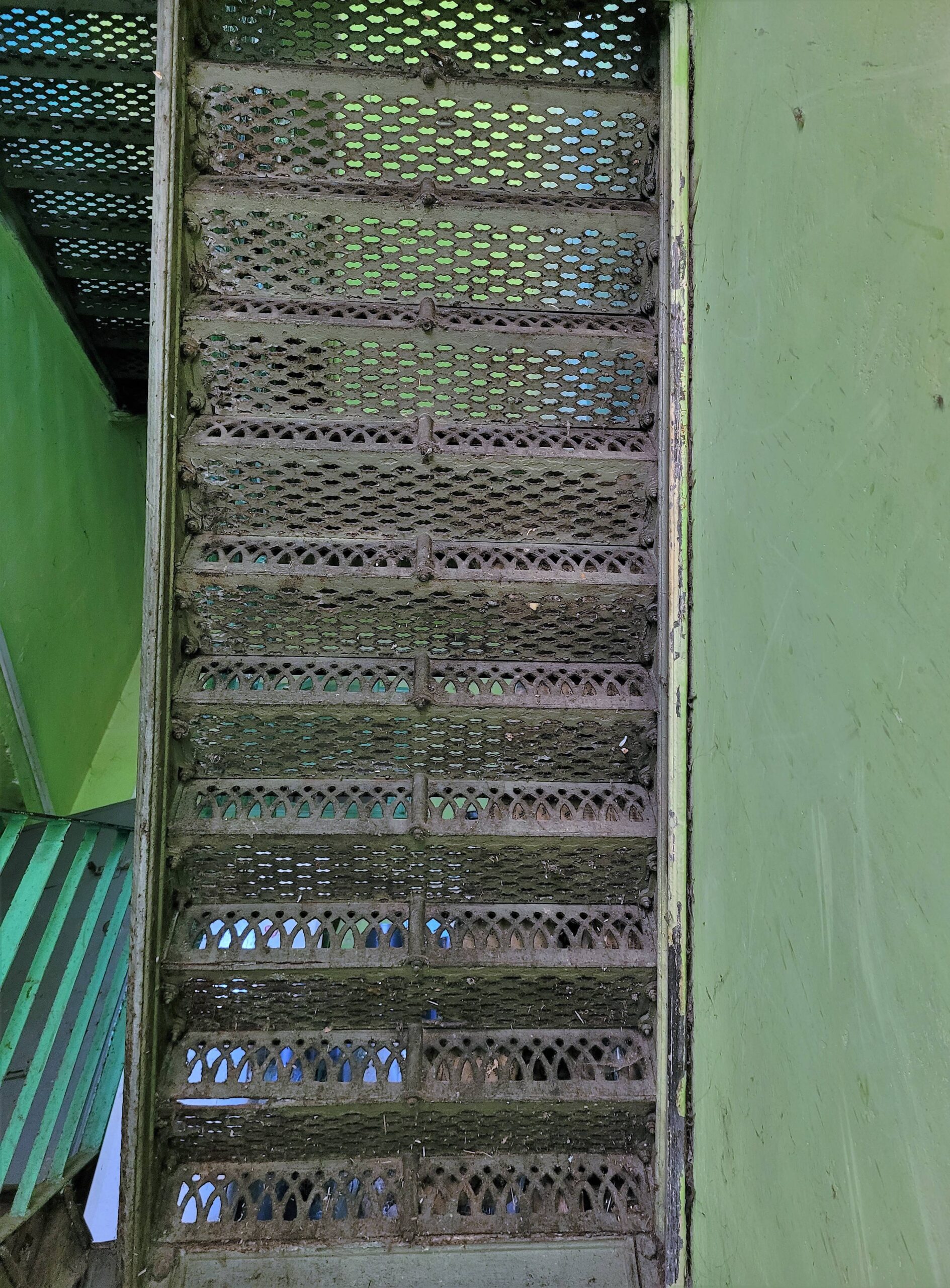 Żeliwne, ażurowe schody na klatce. Ujęcie od spodu. Widać sposób mocowania: na śrubę. Fot. Jerzy Majewski 2022 r., źródło: Res in Ornamento II.